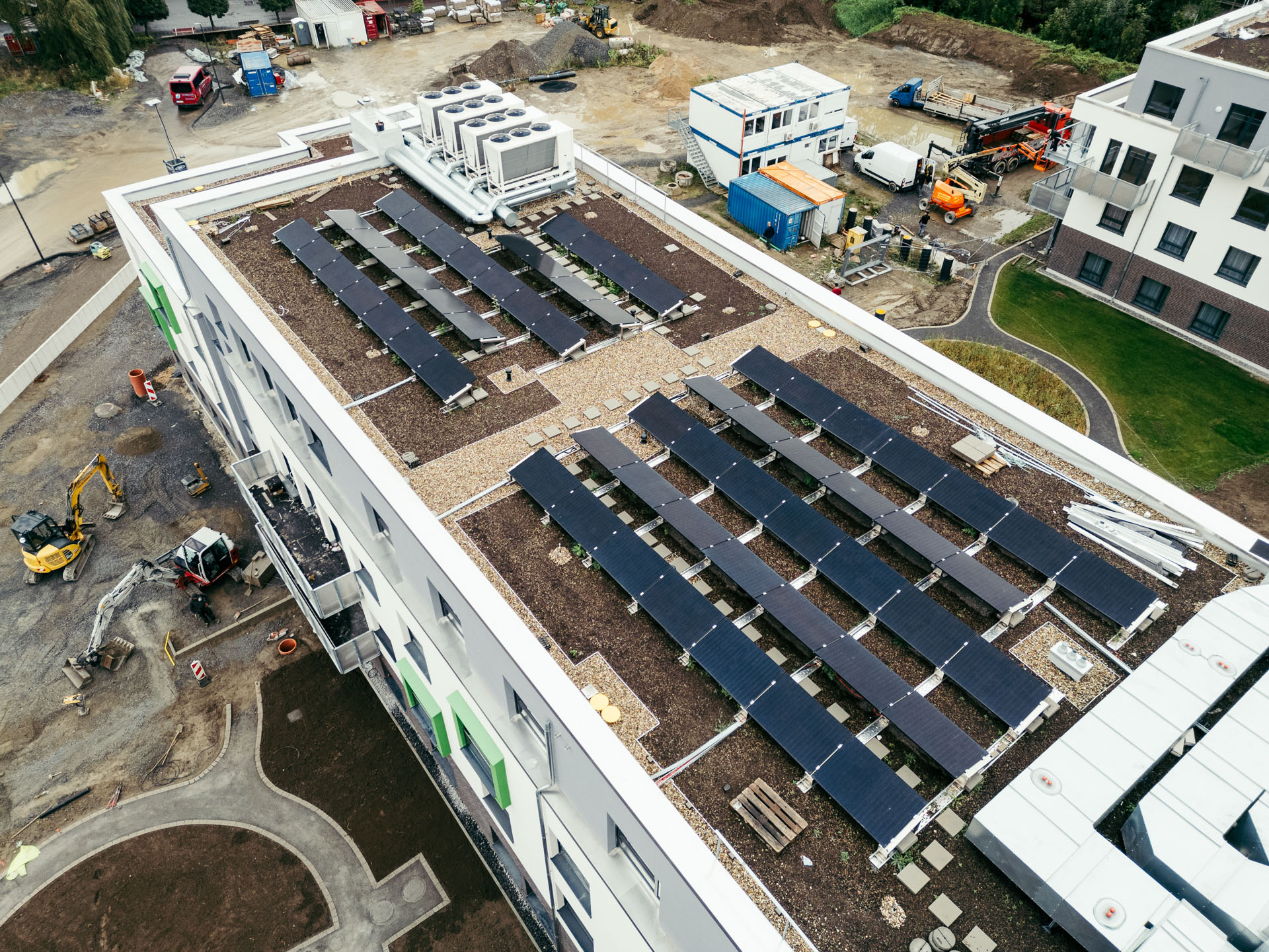 Drohnenaufnahme des Flachdachs des Pflegewohnstifts Gummersbach mit installierten Solarpaneelen in Reihenausrichtung und extensiver Begrünung; im Hintergrund sichtbare Baustelle und Gebäudekomplex.