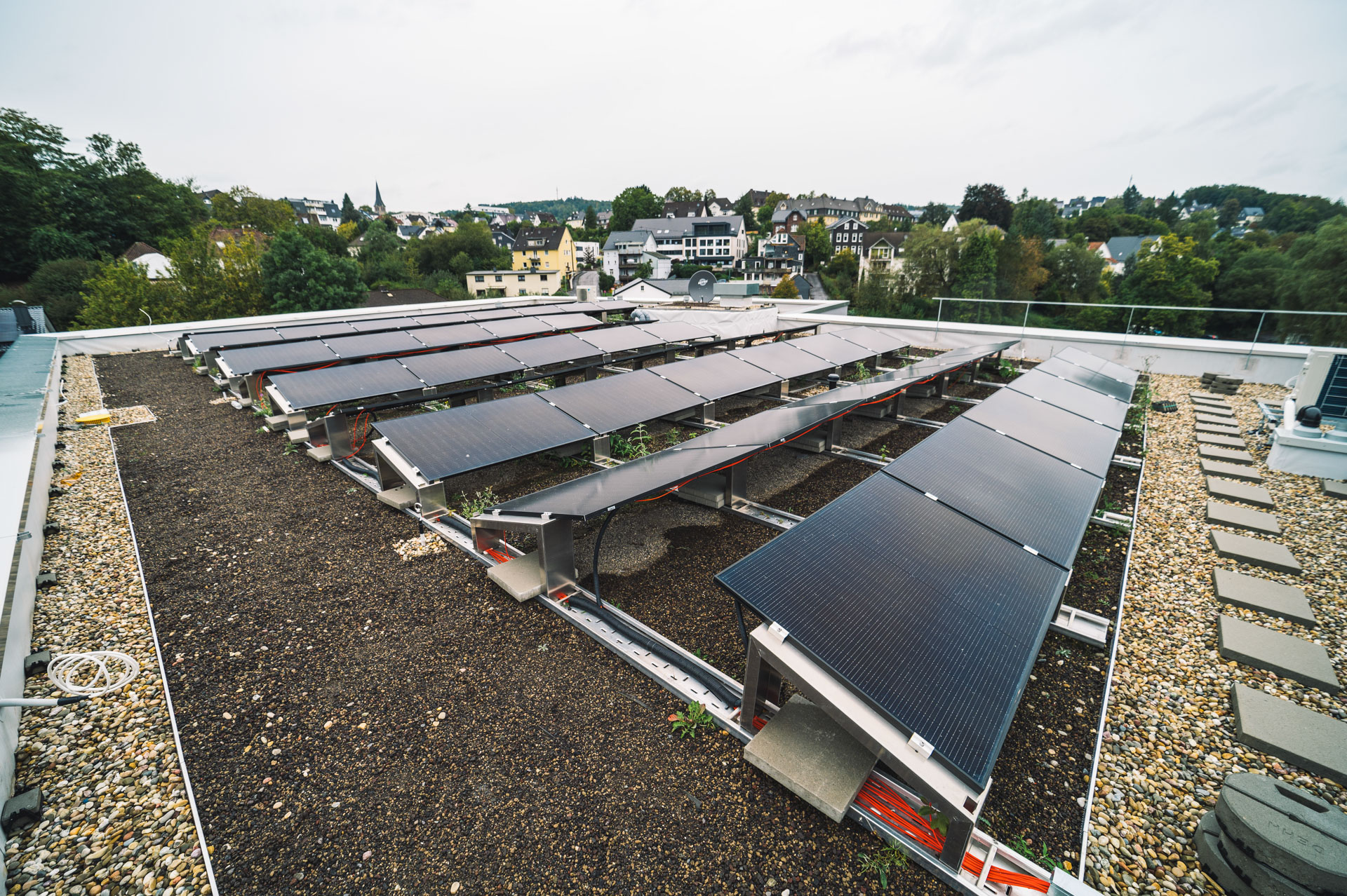 Flachdach mit installierten Solarpaneelen auf Kies- und Substratschicht, mit Blick auf die umliegende Wohnbebauung in Gummersbach; Teil der nachhaltigen Dachlösung des Pflegewohnstifts.