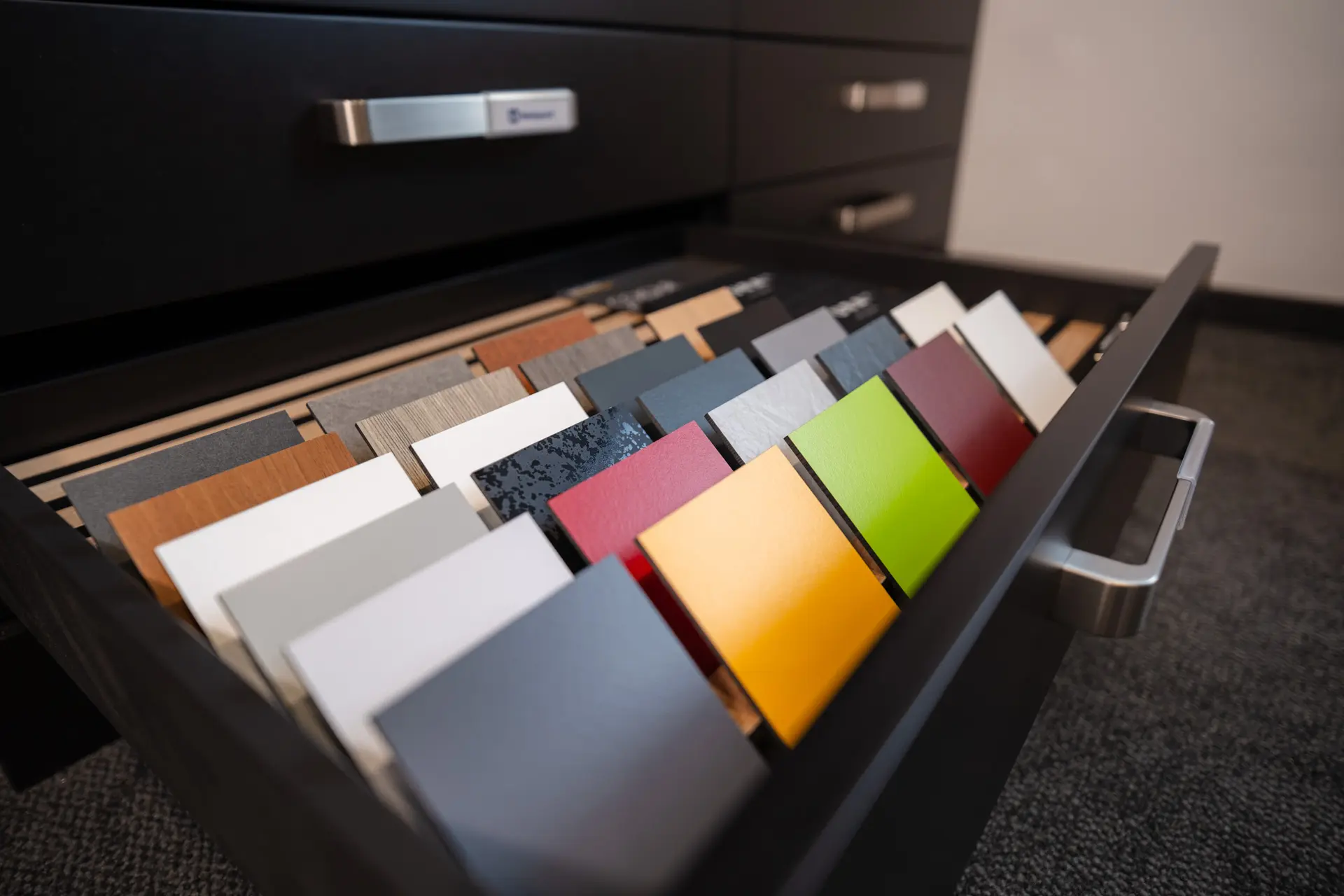 Geöffnete Schublade mit Farb- und Oberflächenmustern von HPL-Platten, sortiert in Reihen. Auswahl moderner Fassadenverkleidungen aus Trespa®.