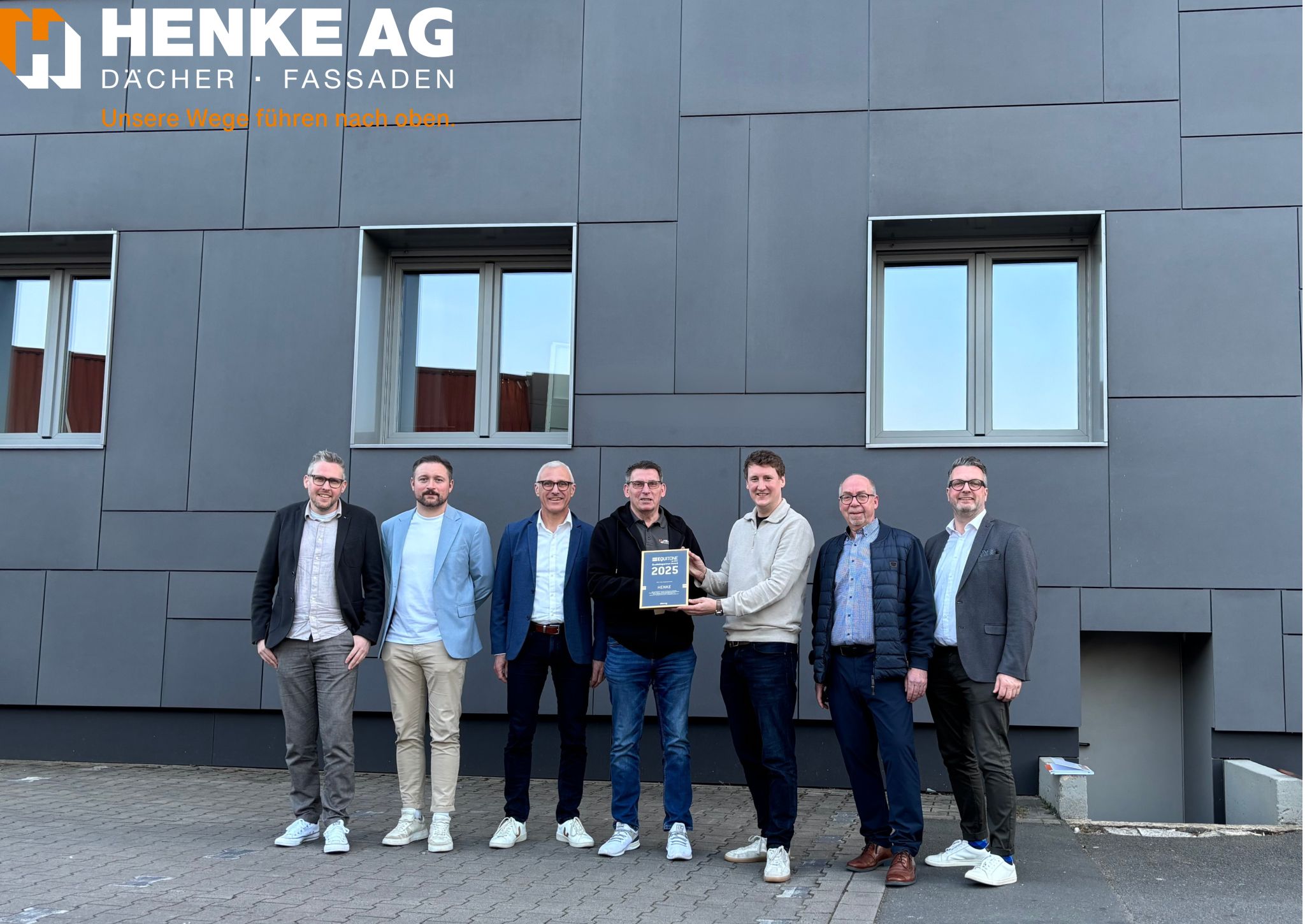 Foto der Verleihung des Equitone Partner Awards an die Henke AG: Zu sehen sind Team-Mitglieder von Equitone mit Henke AG-Vorstand Philipp Brüggemann vor dem Henke AG Standort in Hagen.